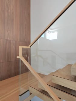 Glass panel with a white oak handrail beside thick floating oak treads against a walnut wall.
