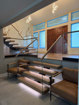 Oak floating treads with underglow LED lighting and glass railing step up from a sunken lounge to a marble-walled entry.