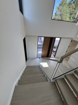 View down a wood stair toward the front door with frameless glass and a wood handrail.