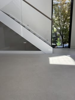A white-stringer floating stair with frameless glass beside a tall window over a pale terrazzo floor.