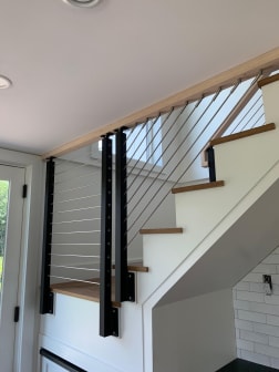 Black posts with stainless cable infill rising along a white stair with oak treads to a wood ceiling header.