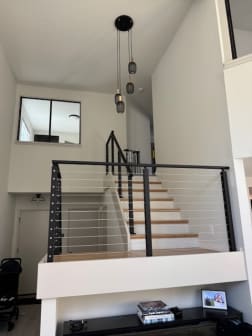 Black-post cable railing with oak treads updates a split-level entry stair beneath tall pendant lights.