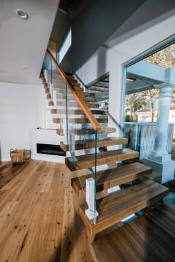 Wood floating treads with frameless glass on white ascend talons and a wood handrail beside a fireplace.