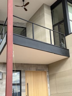 Black cable railing lines a cantilevered balcony above a wood front door on a stone home