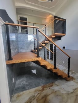 Oak switchback stair with a floating landing and black cable railing beside a slate wall