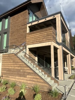 Frameless glass railing follows exterior stairs up the side of a timber-clad home