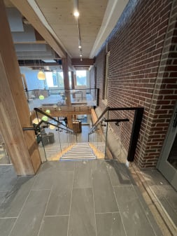 Frameless glass with black handrails around a stair opening beside exposed brick and timber columns