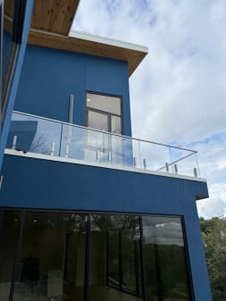 Frameless glass on silver talon spigots wraps a cantilevered balcony on a blue and cedar modern home