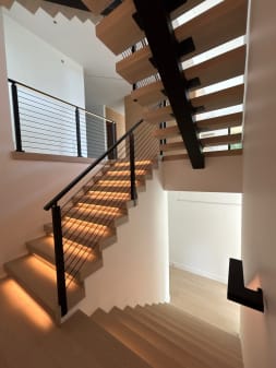 White oak FLIGHT Mono switchback with warm LED tread lighting and black horizontal cable railing