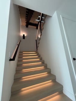 White oak stair treads with warm LED lighting and a black wall-mounted handrail