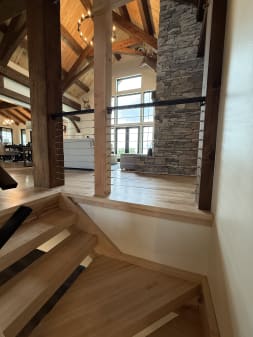Cable railing between wood posts overlooks a timber-frame living room with stone fireplace.