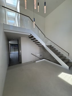 White-stringer floating stair with wood treads and frameless glass in a base rail under a tall bright stairwell.