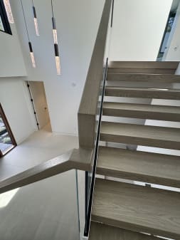 Close view along light oak floating treads with a glass railing and wood handrail.