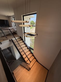 Looking down a black-stringer FLIGHT stair with oak treads and glass railing under a ring chandelier.