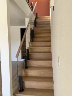 Frameless glass on black Ascend Talons with a white oak handrail lines a closed white oak stair.