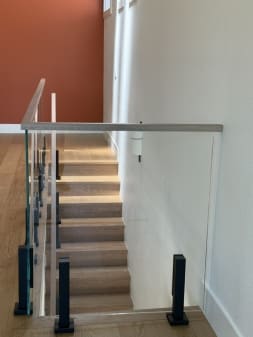 Glass panels on black talons with a white oak cap guard a stair opening beside a terracotta accent wall.