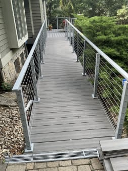 Gray surface-mount cable railing flanks a long composite walkway deck leading to a home.