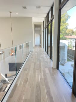 Frameless glass railing in a white base rail lines an upper hallway beside floor-to-ceiling windows.
