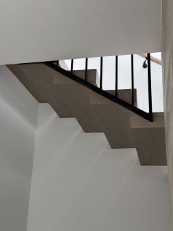 Zig-zag underside of a gray oak stack stair with black vertical balusters and wall handrail.