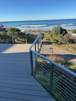Brushed stainless posts and top rail with horizontal cable infill line a composite deck walkway overlooking the ocean surf.
