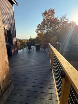 Wood posts and cap rail with cable infill line a long composite deck under autumn trees.