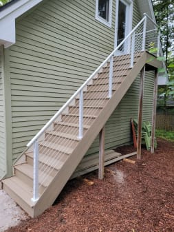 White posts and top rail with cable infill along a composite exterior stair beside sage-green siding.