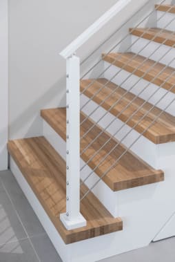 Thick oak treads wrap the bottom steps beside a white newel post with angled cable infill.