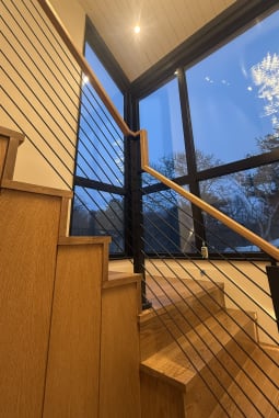 Oak stair with onyx black rod railing and wood handrail beside floor-to-ceiling windows at dusk