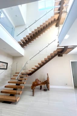 Looking up a wood mono-stringer floating stair with glass railing and a glass-railed loft above.
