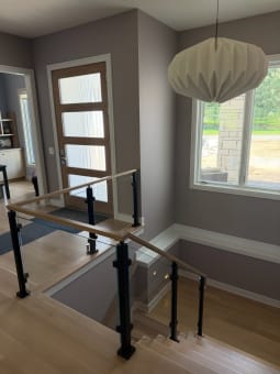 Black-post glass railing with white oak handrail guards a stair opening near a front door.