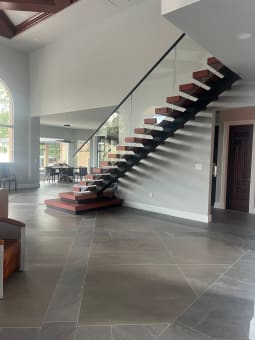 Long black mono stringer stair with red-toned treads, frameless glass guard and plinth steps over large slate tile.