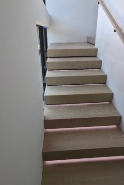 Looking up an oak stair with LED tread lighting and a wall-mounted handrail