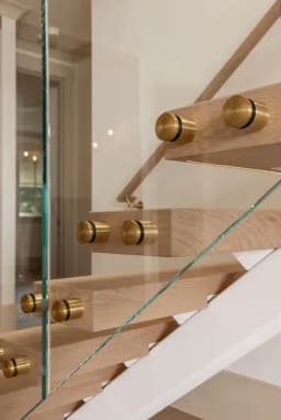 Brass standoff pins anchor clear glass to light oak treads beside a white plaster stringer.
