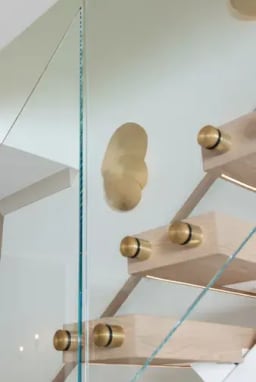 Brass standoff pins and glass along oak treads with a brass wall sconce behind.