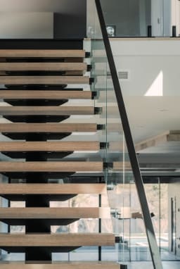 Looking up beneath oak treads on a black mono stringer with standoff-pin glass and a handrail.
