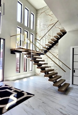 Floating oak switchback stair with frameless glass and a brass handrail in a tall marble foyer