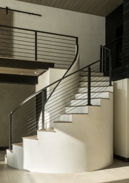 Black horizontal rod railing sweeps around a sculptural curved white plaster stair with dark wood treads.