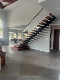 Red-stained floating treads on a black mono stringer start from stacked plinths with glass railing in a tiled great room.