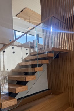 Floating oak treads on a FLIGHT stringer with frameless glass and wood handrail beside a wood slat screen