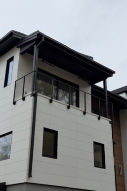 Upper-story balcony with black horizontal rod railing on a white-paneled modern home