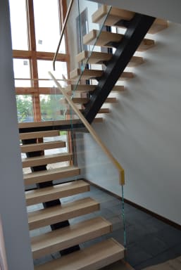 Maple floating treads on a black mono stringer with frameless glass and a maple handrail by tall windows