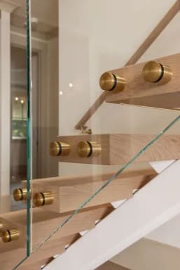 Brass standoff pins anchor clear glass to light oak treads beside a white plaster stringer.