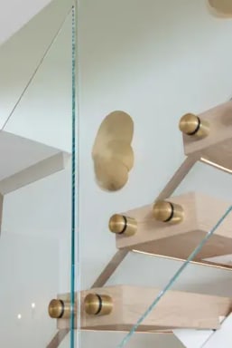Brass standoff pins and glass along oak treads with a brass wall sconce behind.