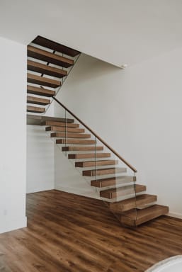 Warm wood cantilever treads float off a white wall with frameless glass and wood handrail above wood flooring.