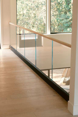 Frameless glass in a black base rail with a light wood handrail along an upper hallway with forest views.