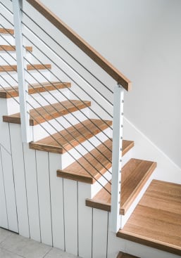 Natural oak treads on a white shiplap stair with white posts, cable infill and a wood cap rail.