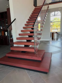 Red-stained stacked plinth boxes at the base of a FLIGHT mono stair with frameless glass railing.