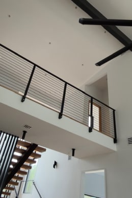 Interior balcony with black horizontal rod railing above a floating stair