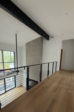 Black horizontal rod railing lines an oak-floored loft under a black beam