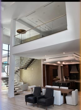 Floating stair and glass-railed loft above a dining and lounge area with modern pendants